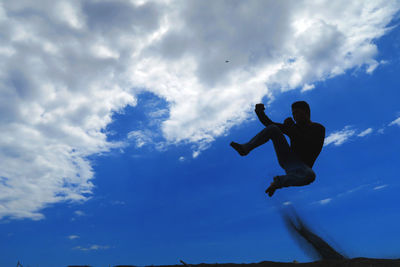 Low angle view of man jumping against sky