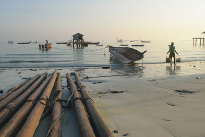 People working on boat moored at shore against sky