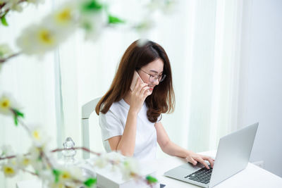 Young woman using phone while sitting on table