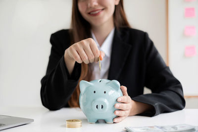 Midsection of businesswoman putting coin in piggy bank