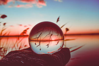 Close-up of crystal ball against lake during sunset