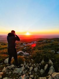 Man standing on rock against sky during sunset