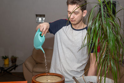 A young man spills water from a watering can on the ground. transplanting  a plant
