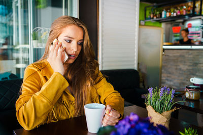 Shocked young woman using mobile phone while sitting in cafe