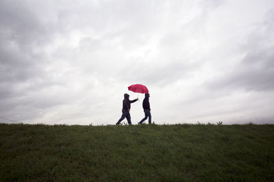 Two men walking on grassy field against cloudy sky