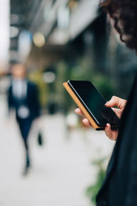 Cropped image of businesswoman using smart phone in city
