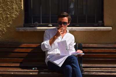 Man smoking cigarette while holding book on bench