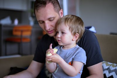 Little toddler eating banana held by his father