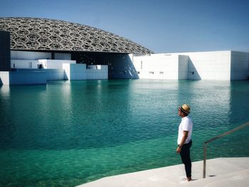 Rear view of man standing at swimming pool against clear sky