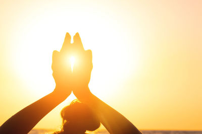 Silhouette woman holding yellow flower against orange sky