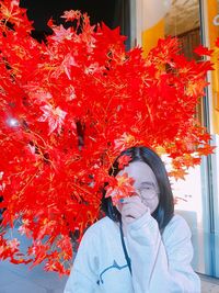 Portrait of young woman standing by red flowering plant