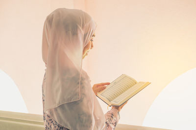 Side view of woman reading book against wall