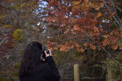 Woman photographing by tree during autumn