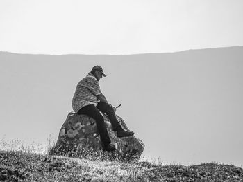 Woman sitting on field against clear sky