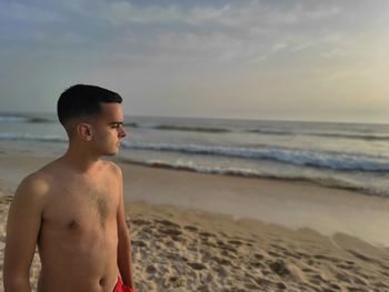 Young man standing at beach against sky