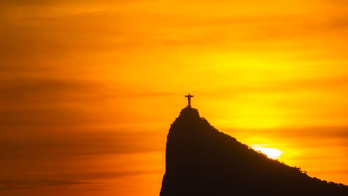 Silhouette of cross against cloudy sky during sunset