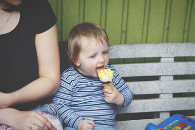 Midsection of mother by son eating ice cream on bench