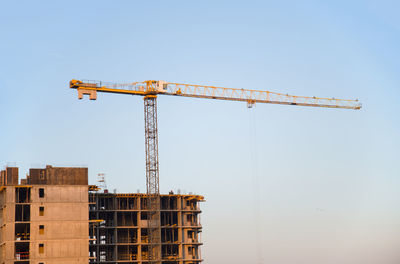 Low angle view of crane on building against clear blue sky
