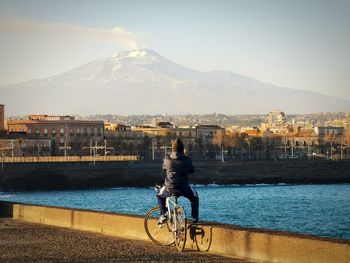 Man riding bicycle on city by buildings against sky