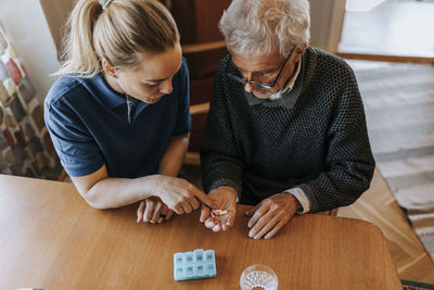 High angle view of female caregiver explaining medicine dose to senior man at home