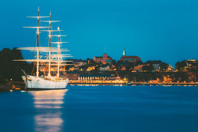 Sailboats in sea against illuminated buildings in city at night