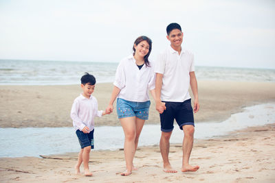 Family holding hands while walking at beach against sky