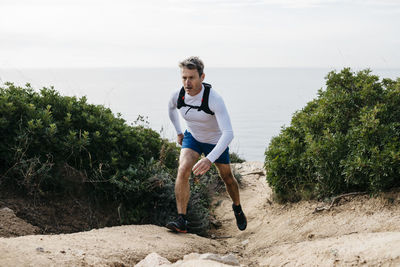 Man walking on dirt road amidst bushes against clear sky