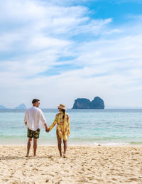 Rear view of woman standing at beach against sky