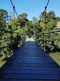 Footbridge amidst trees against clear sky