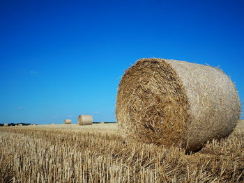 Hay bales on field against clear blue sky