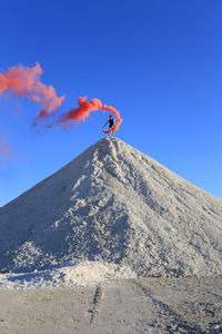 Low angle view of teenage boy holding distress flare standing on mountain against sky