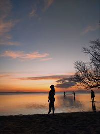 Silhouette woman walking at beach against sky during sunset