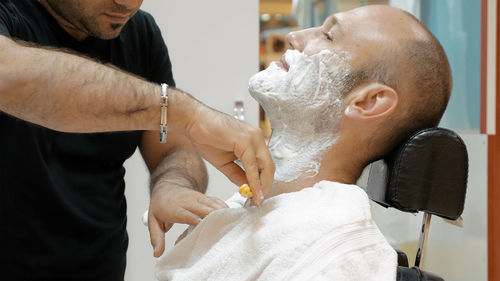 Midsection of barber doing shaving of mature man in salon