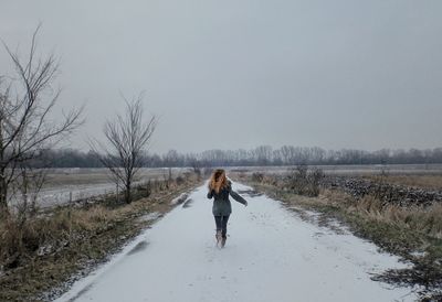 Rear view of woman running on snow covered road against sky