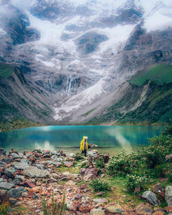 Rear view of man standing by lake against mountain