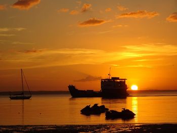 Silhouette boats moored on sea against orange sky