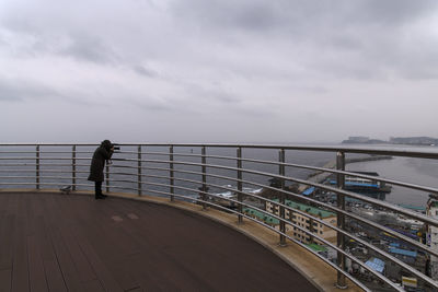 Rear view of man standing on railing against sea