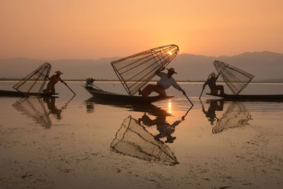 Fishermen fishing in lake against sky during sunset