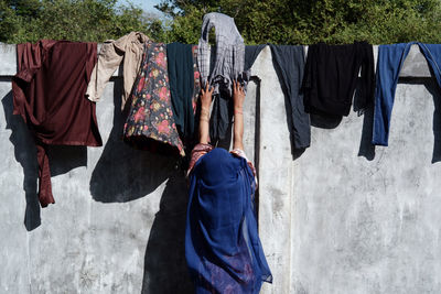 Rear view of woman standing against wall to drying clothes