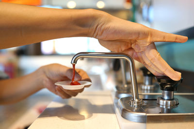 Cropped image of person pouring tomato sauce in cup