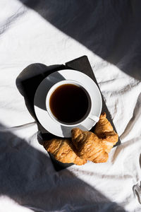 Coffee cup and croissants on the bed in morning sunlight. trendy still life with interesting shadow.