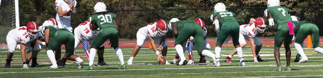 Two high school football teams lined up in the shotgun ready to start a play on a green turf field.