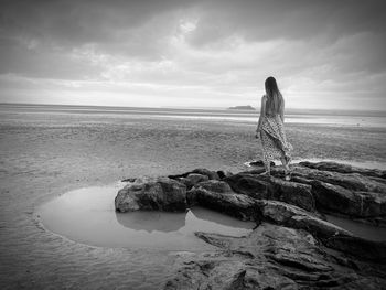 Rear view of woman standing on rock against sea and sky
