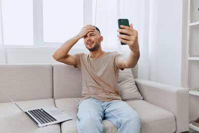 Young woman using phone while sitting on sofa at home