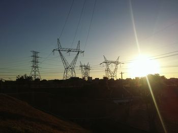 Silhouette electricity pylons on field against sky at sunset