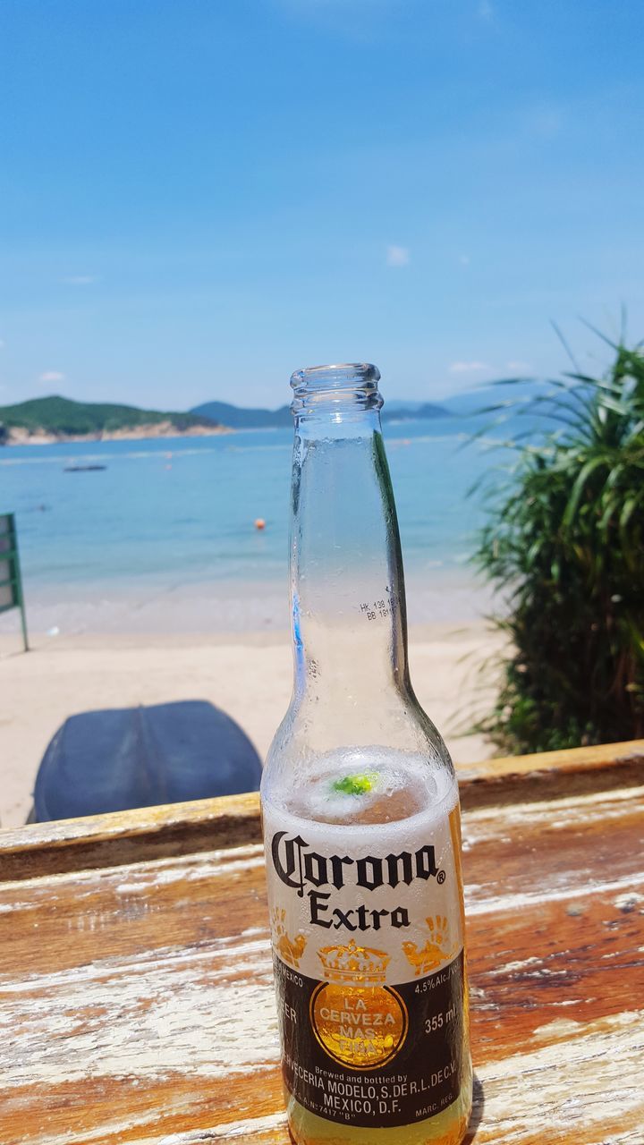 text, western script, water, beach, sea, day, no people, bottle, communication, sand, nature, outdoors, close-up, table, drink, sunlight, sky