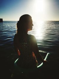 Woman sitting in sea against sky