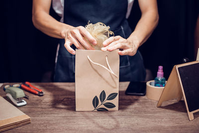 Midsection of woman packing gift on table