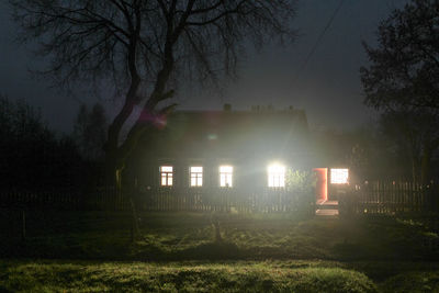 Illuminated building by trees against sky at night