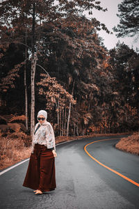 Full length of woman standing on road against trees